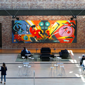 Indoor lounge space with tables, seating, and a colorful Disney-themed mural displayed on a brick wall