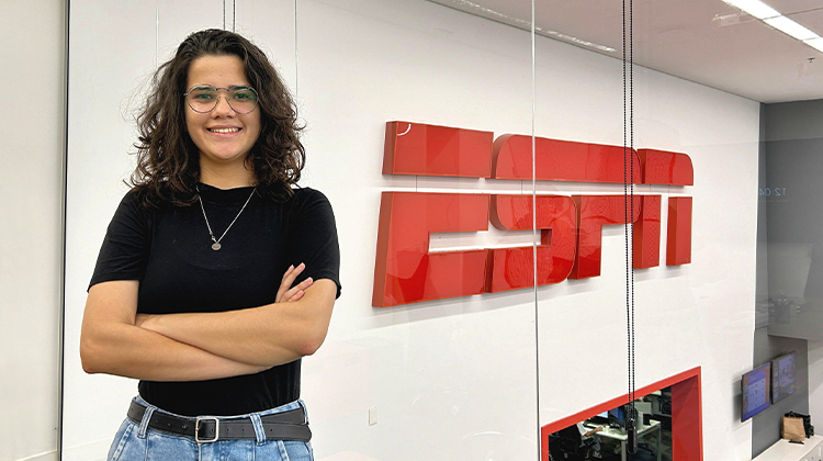 Brazil Apprentice Nicolle smiling wearing a black shirt and jeans standing in front of an ESPN sign