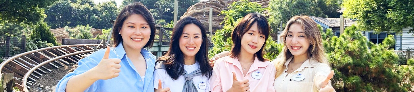 Four interns smiling and waving in front of an attraction in Hong Kong Disneyland Resort