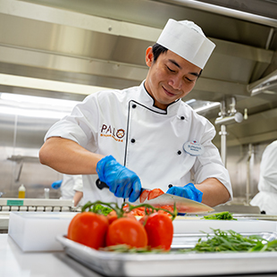 male chef in a white uniform, smiling and chopping vegetables