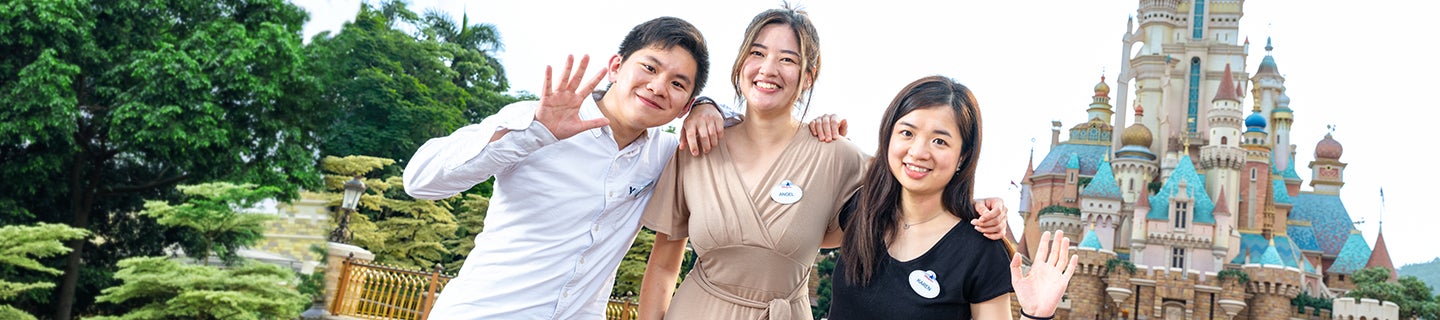 Three interns smiling and waving in front of a Cinderella's Castle in Hong Kong Disneyland Resort