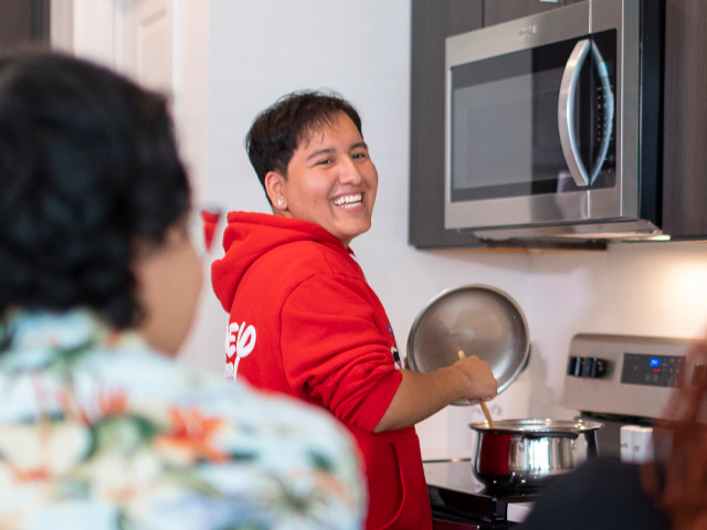 A smiling person cooks in a kitchen