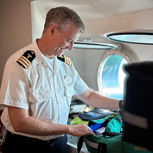 male physician unzipping a medical bag in front of a ship porthole