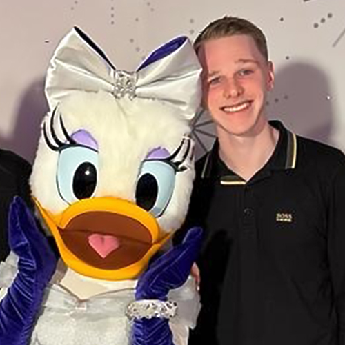 Disney UK Intern Callum, wearing a black polo and smiling with Daisy Duck