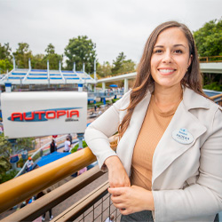 A smiling woman stands with the Autopia ride and sign in the background