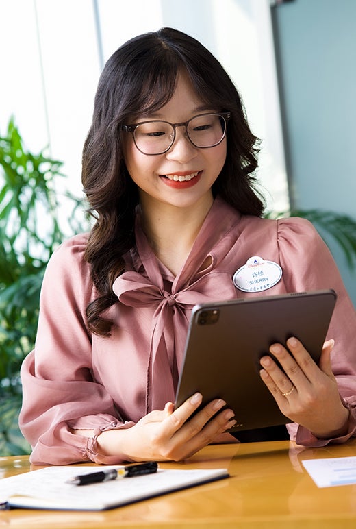 Asian female in business attire, smiling and looking at a tablet