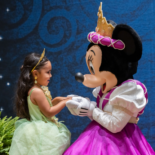 Minnie Mouse dressed as a princess, facing and holding the hands of a little girl dressed like a princess