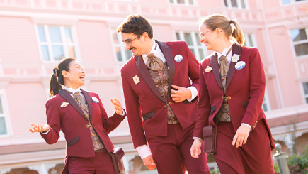 Three colleagues in red suits conversing and laughing in front of a pink building