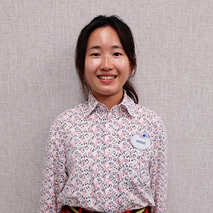 Female Hong Kong Disneyland Disney College Program participant with dark brown hair tied back wearing a colorful button down shirt smiling