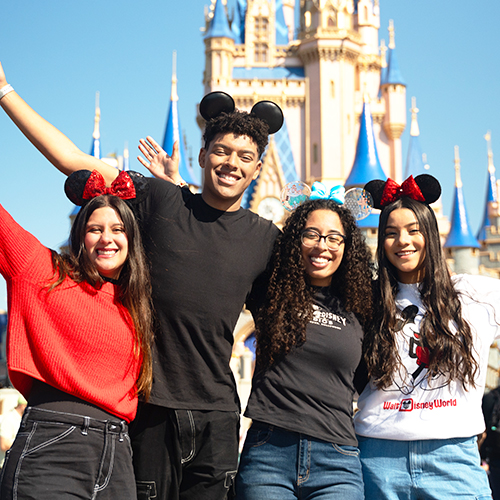 Cuatro participantes del Programa de Intercambio Cultural Disney LATAM con orejas de Minnie y Mickey sonriendo frente al Castillo de Cenicienta en Walt Disney World