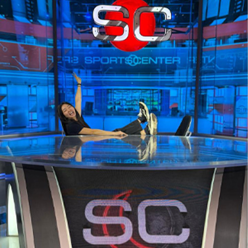 Person posing on the SportsCenter studio desk in front of the SportsCenter set