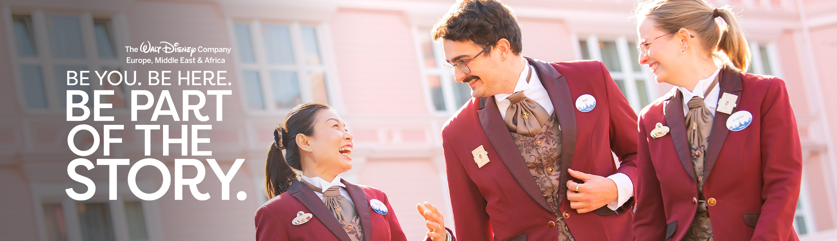Three colleagues in red uniforms laughing in front of a pink building