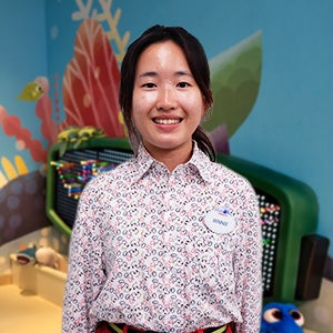 Female Hong Kong Disneyland Disney College Program participant with dark brown hair tied back wearing a colorful button down shirt smiling