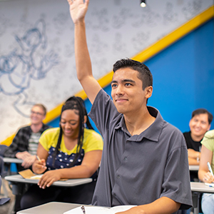 Young man raising his hand to answer a question in a Disney classroom.