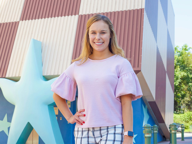 Smiling woman in a pink top against a checkered building and blue star