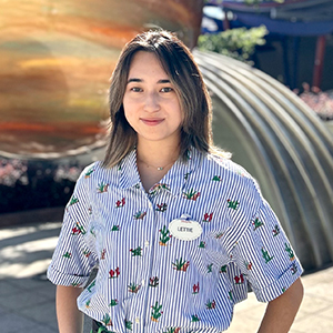 Hong Kong Disneyland Resort Intern Lettie with short light brown hair and a colorful shirt smiling in front of a park attraction