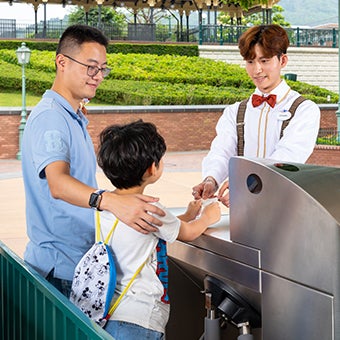 Male Hong Kong Disneyland cast member wearing suspenders and a bow tie helping a family at the park's entrance