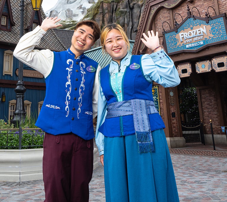 pair of colleagues in costumes waving in front of the Frozen Ever After ride at Hong Kong Disneyland Resort