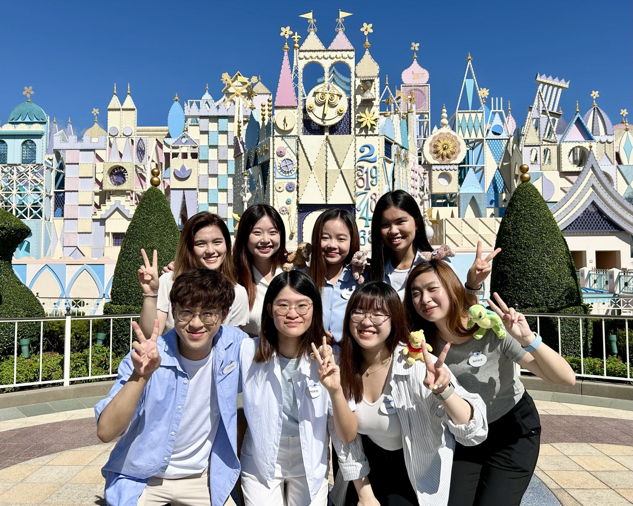 Group of Disney Interns smiling in front of the It's a Small World attraction at Hong Kong Disneyland