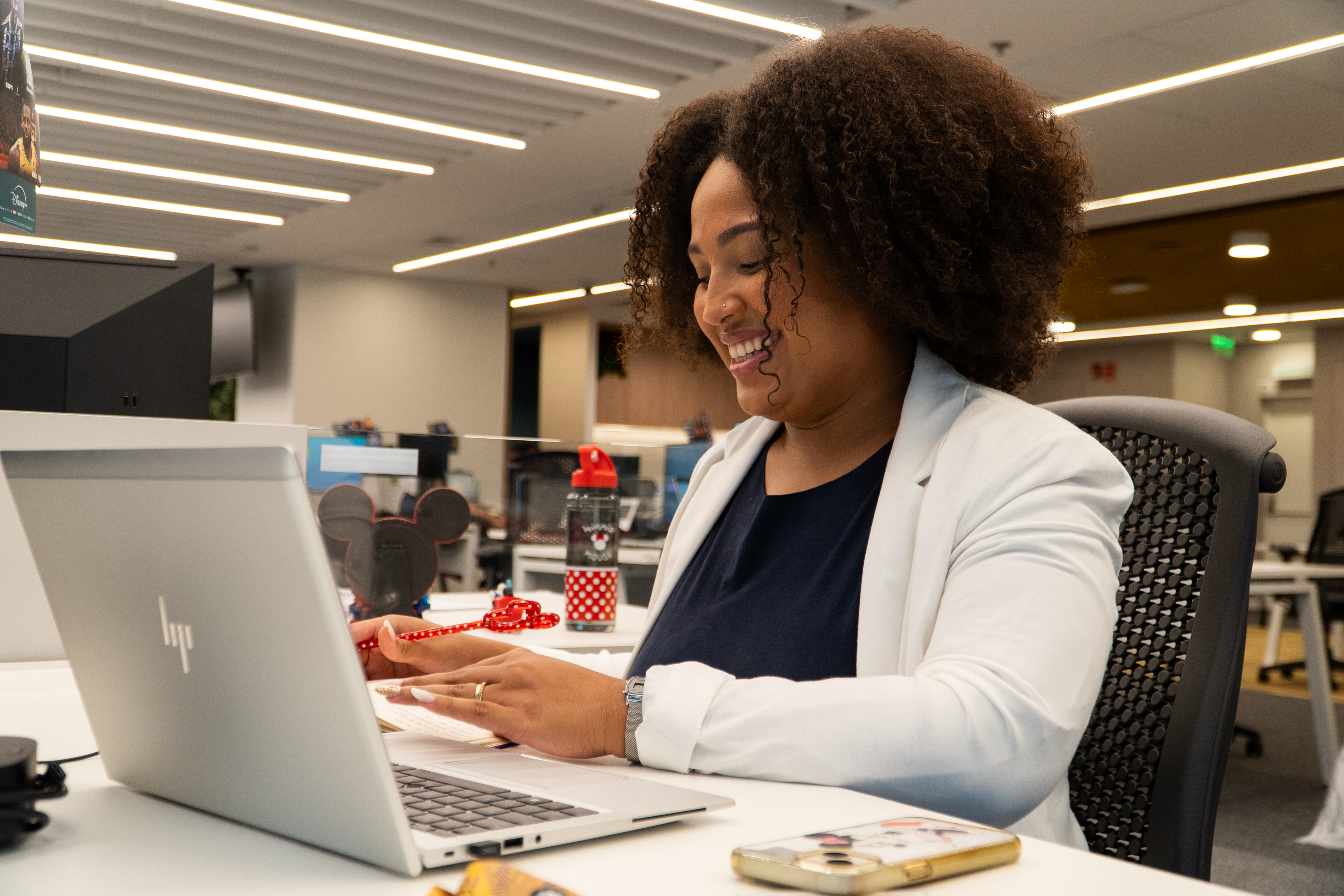 Black woman smiling working on a laptop in an open office setting