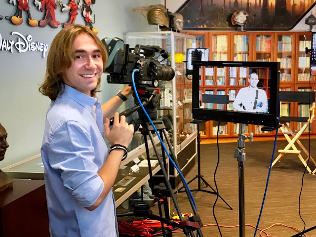 A smiling videographer operates a camera in a Disney-themed production setting