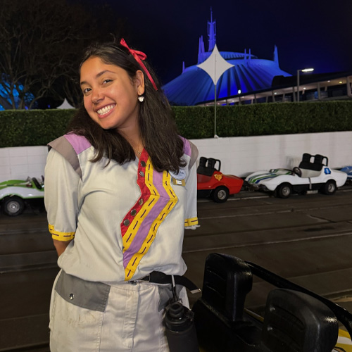 Person standing beside parked vehicles in an outdoor entertainment area at night