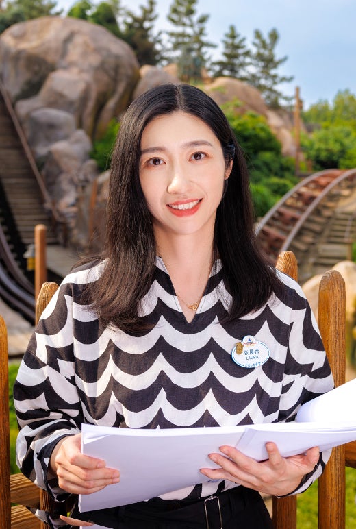 smiling female employee in business attire, standing in front of a Disney park attraction