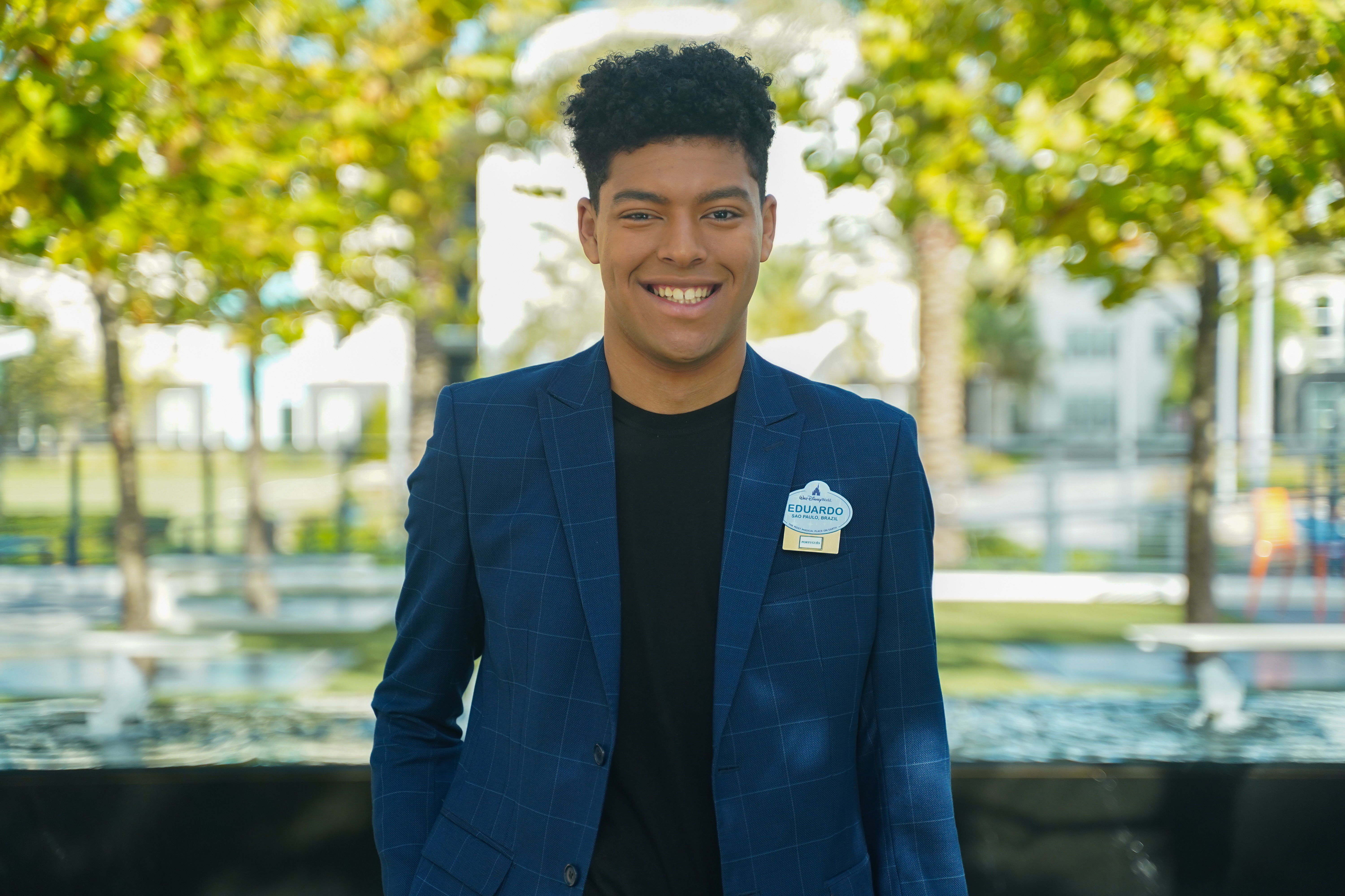 Male Brazil Apprentice with short curly black hair smiling while wearing a black shirt and navy blazer