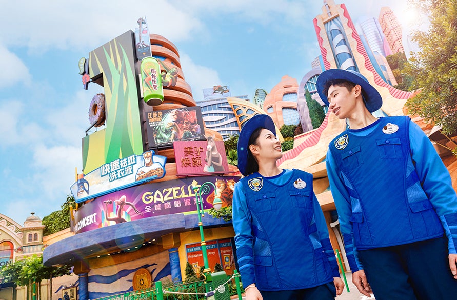 two young Disney park employees in uniform, with a colorful Disney park in the background