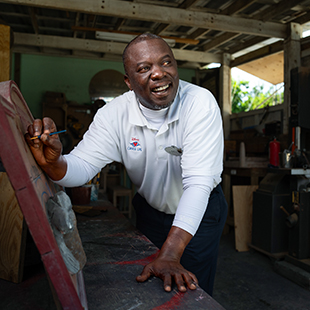 black male DCL employee in uniform inside a workshop, painting and smiling