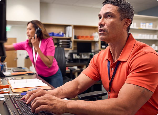 Two pharmacists working on computers, one on the phone