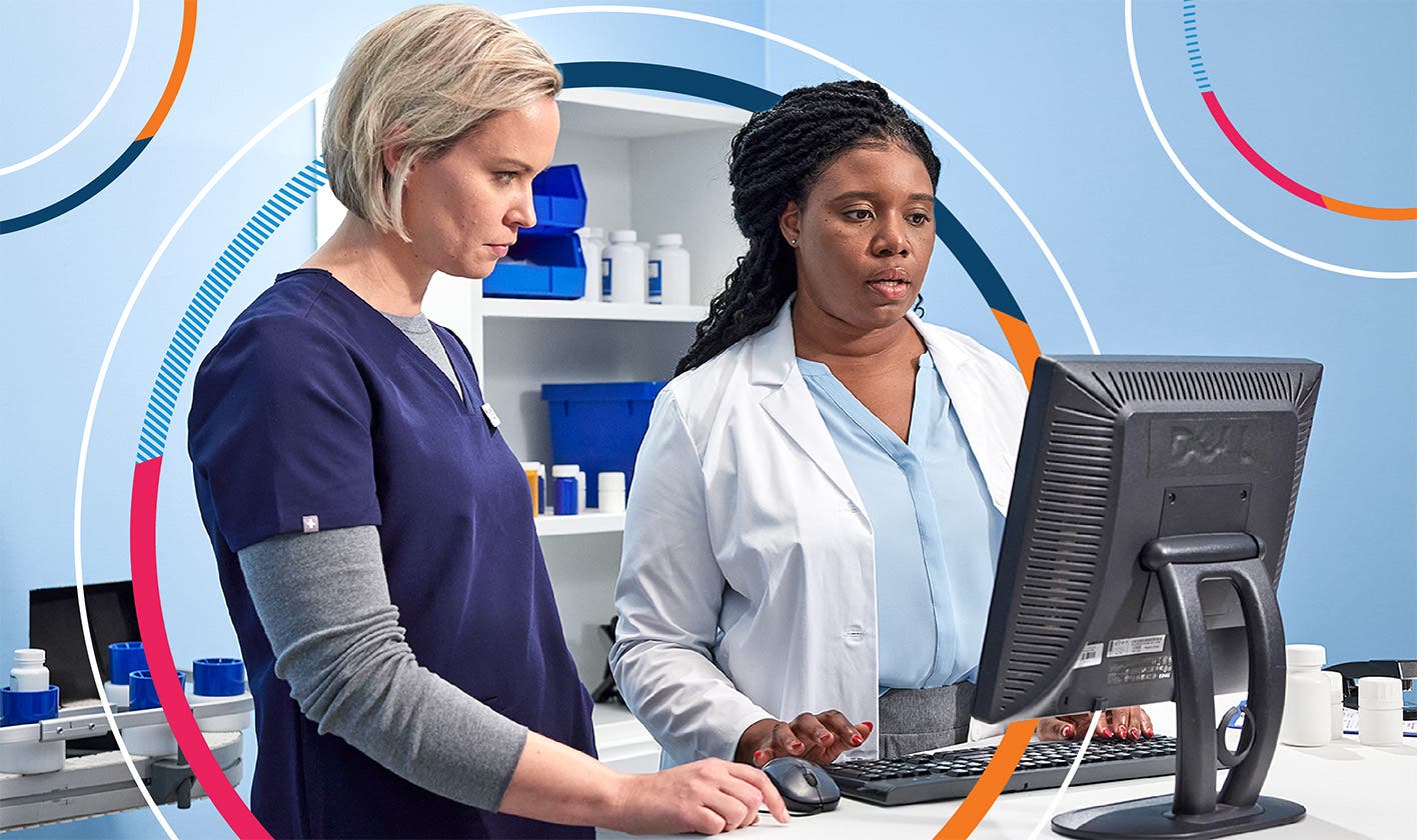 Two pharmacists reviewing a computer monitor in a pharmacy setting.