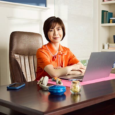 Woman sitting in an orange top at a desk in front of a computer