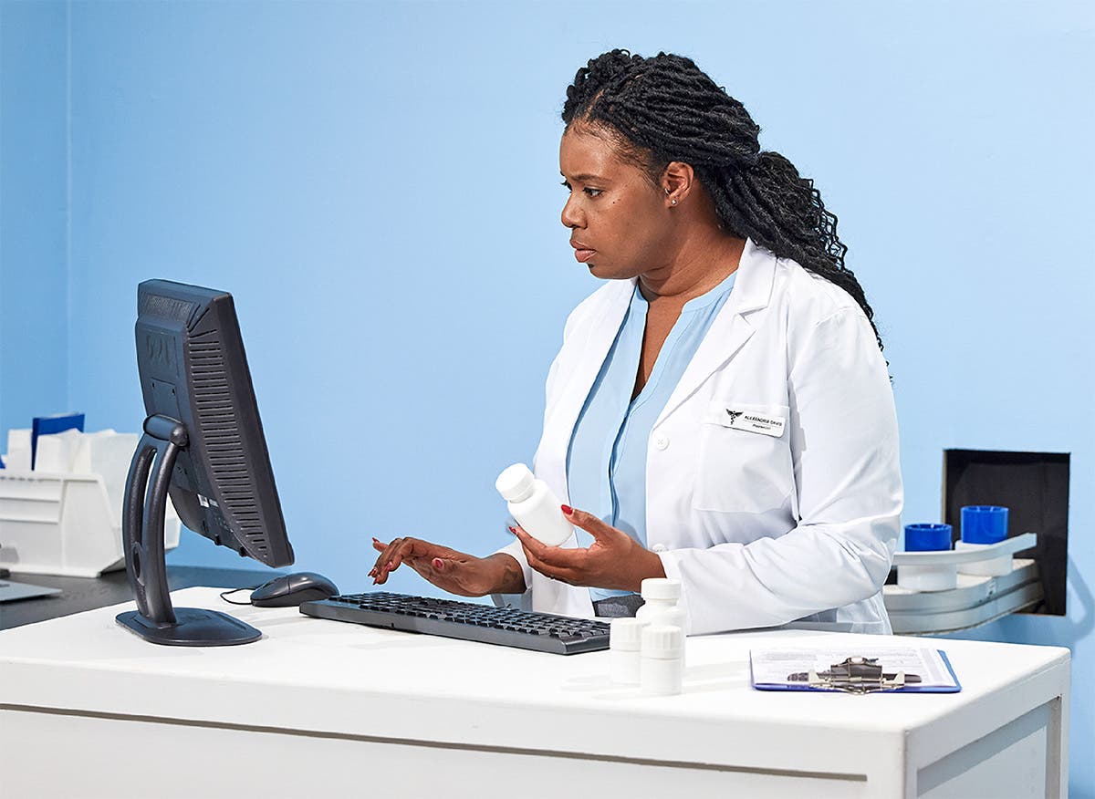 Pharmacist at workstation looking at information on the computer while holding a bottle of medication.