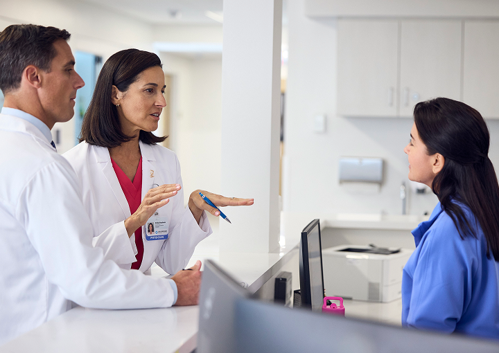 A nurse and a doctor consulting one another in front of a computer in a doctor's front office