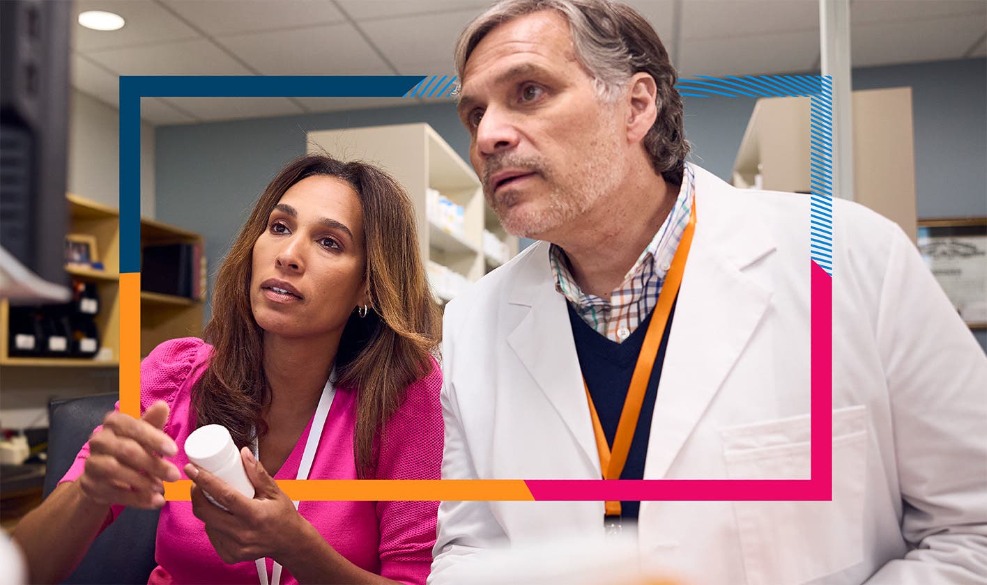 Two pharmacists review a computer screen in a pharmacy setting