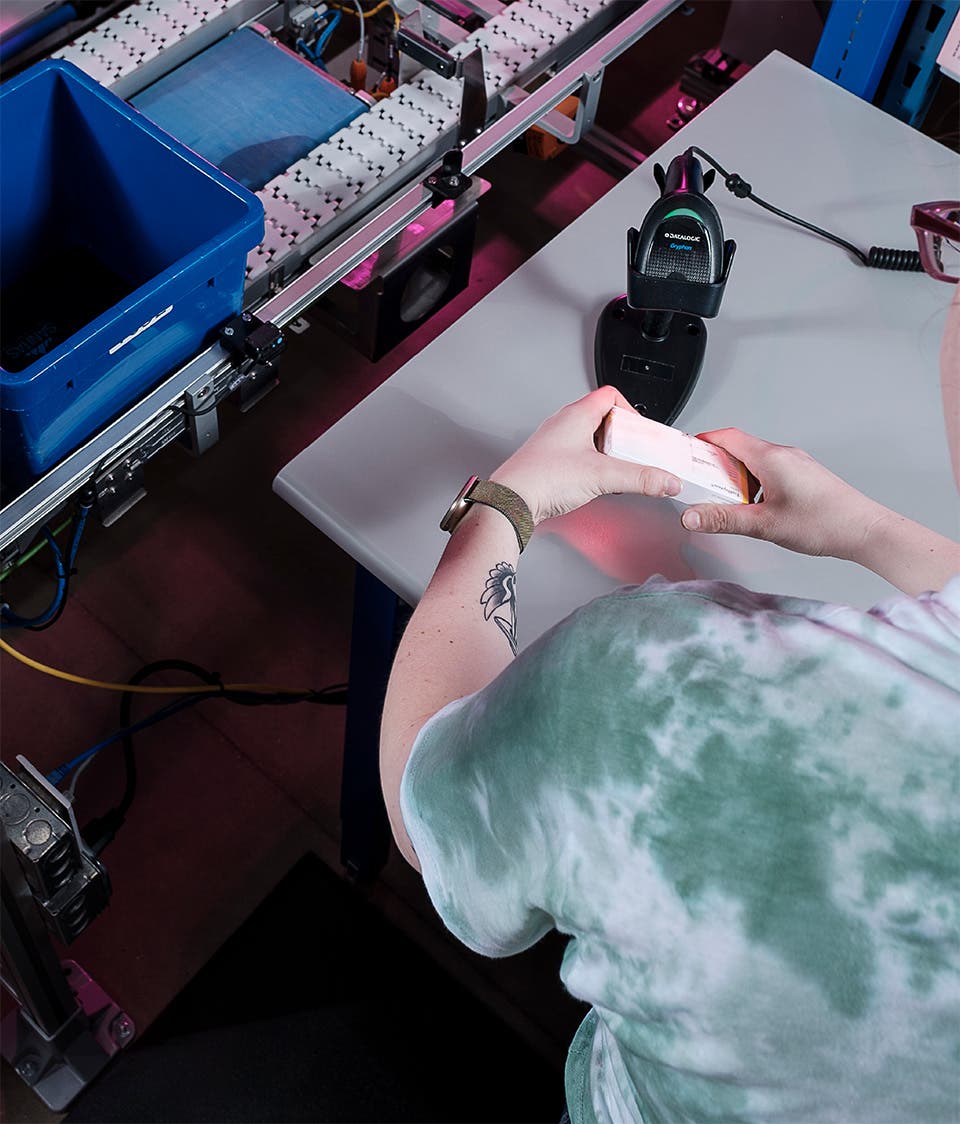 Worker at a central fill facility scanning a box of medication for dispense