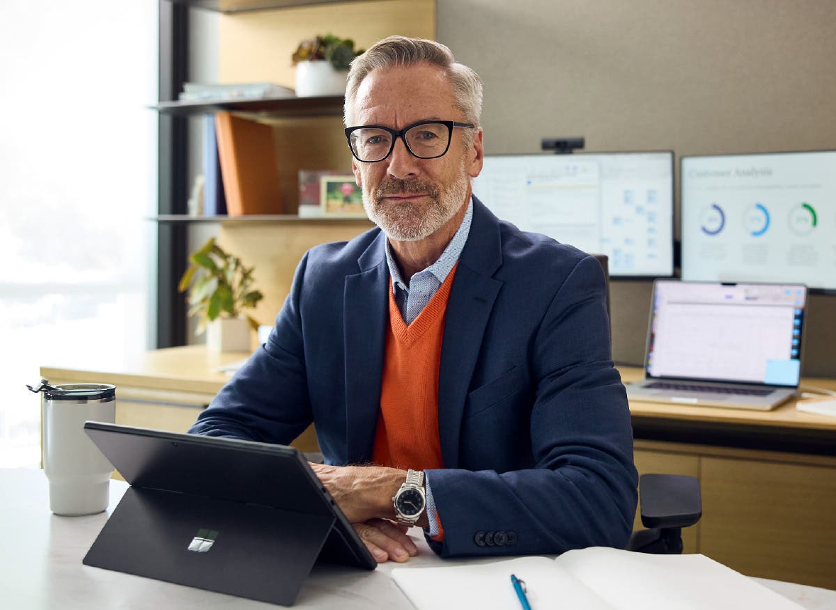 Male executive seated at an office table reviewing data on a tablet.