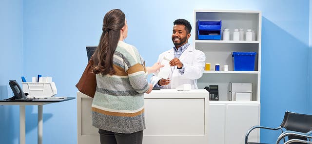 Image of a pharmacist handing a prescription to a patient at a pharmacy counter