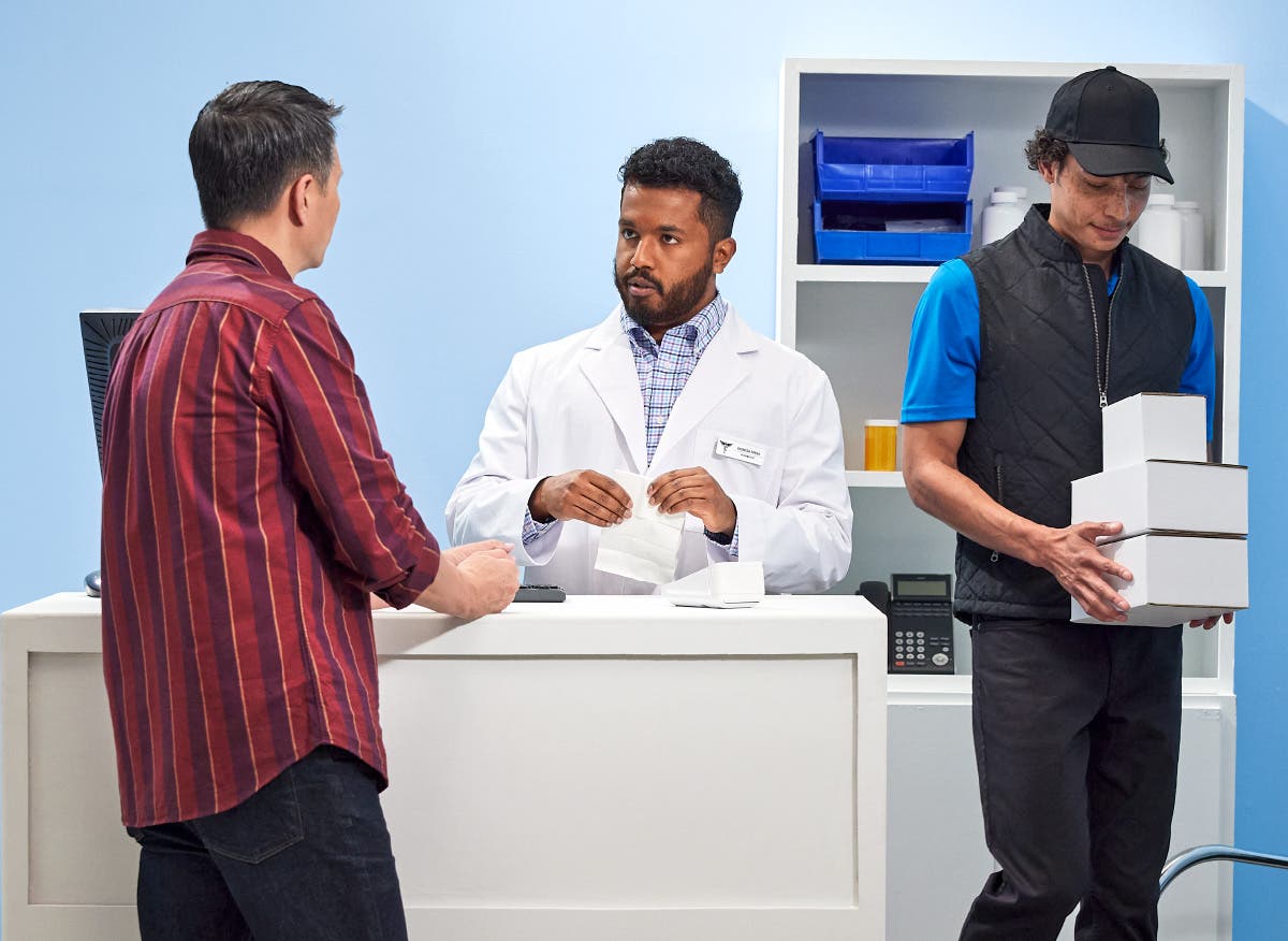 Pharmacist educating a patient about a prescription while a delivery person grabs packages