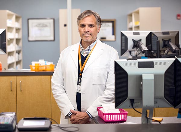 A pharmacist standing in front of a computer in a white lab coat