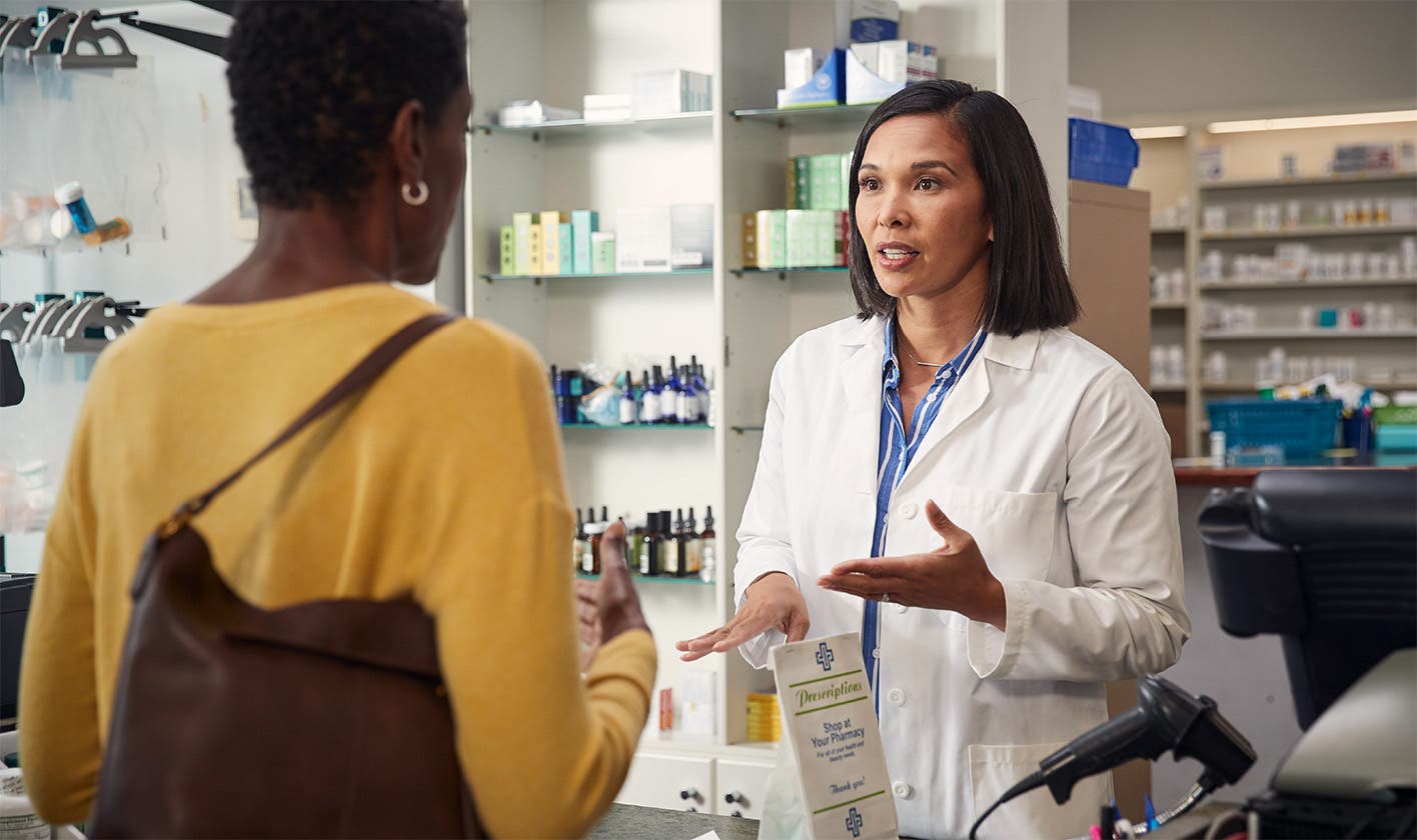 A pharmacist at the pharmacy counter hands two bags of medication to a patient.