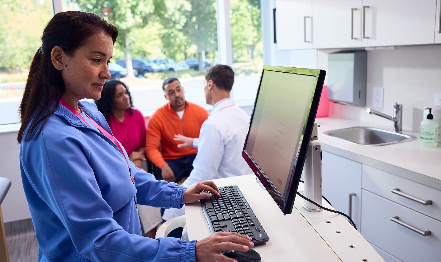 Care team member completing a prior authorization while patients discuss with provider in background.