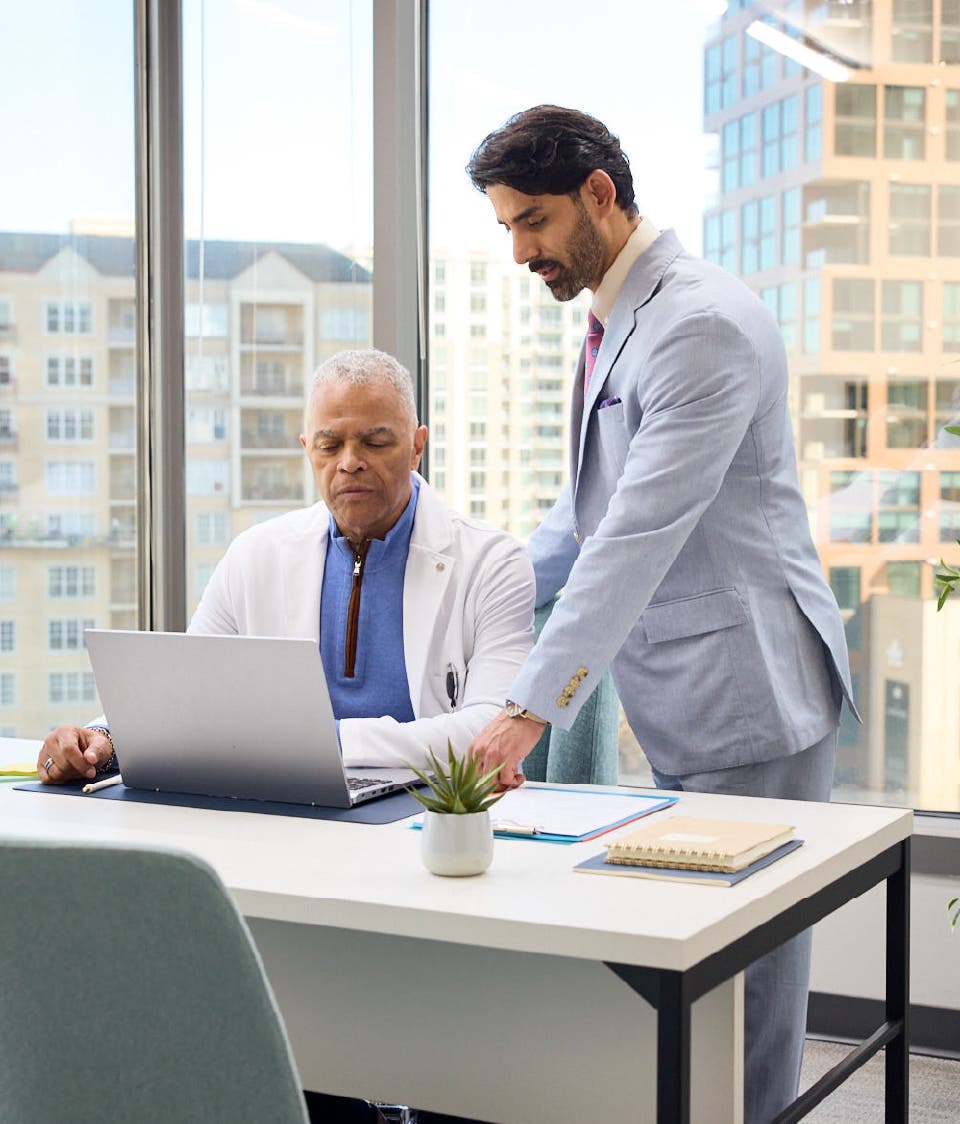 A FRM standing next to a sitting provider, consulting him on a laptop