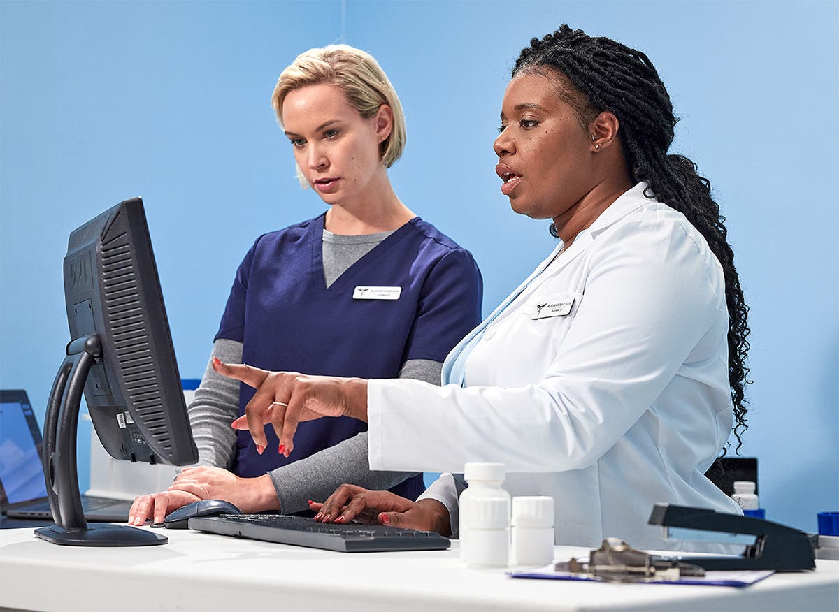 Two pharmacists reviewing information on workstation computer monitor in a pharmacy setting.