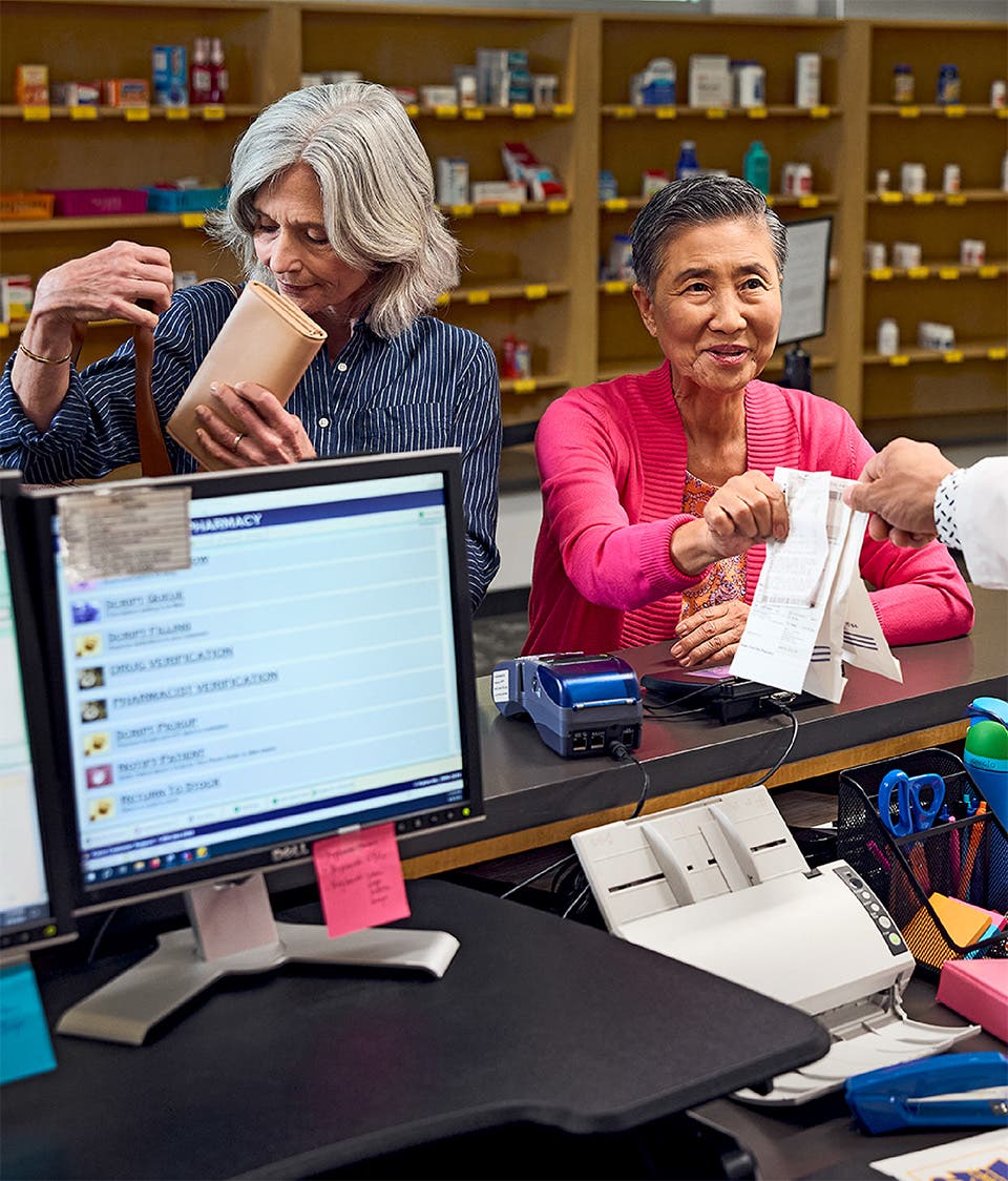 Patient receiving medication from a pharmacist while spouse puts wallet away.