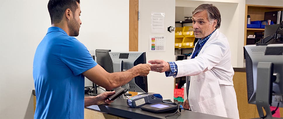 Patient at the pharmacy counter handing insurance card to pharmacist.