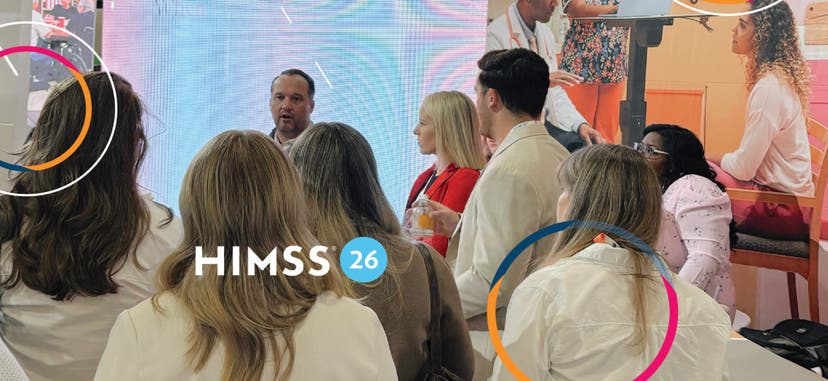 A handful of folks standing together at the HIMSS Conference listening to a speaker