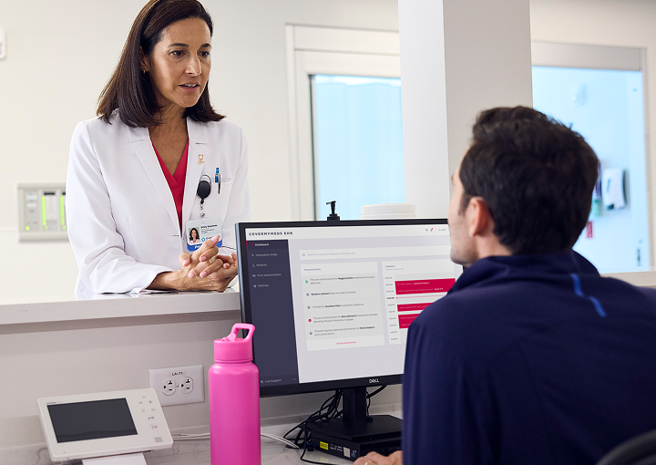 A provider standing at a counter chatting with another provider who is sitting at a computer