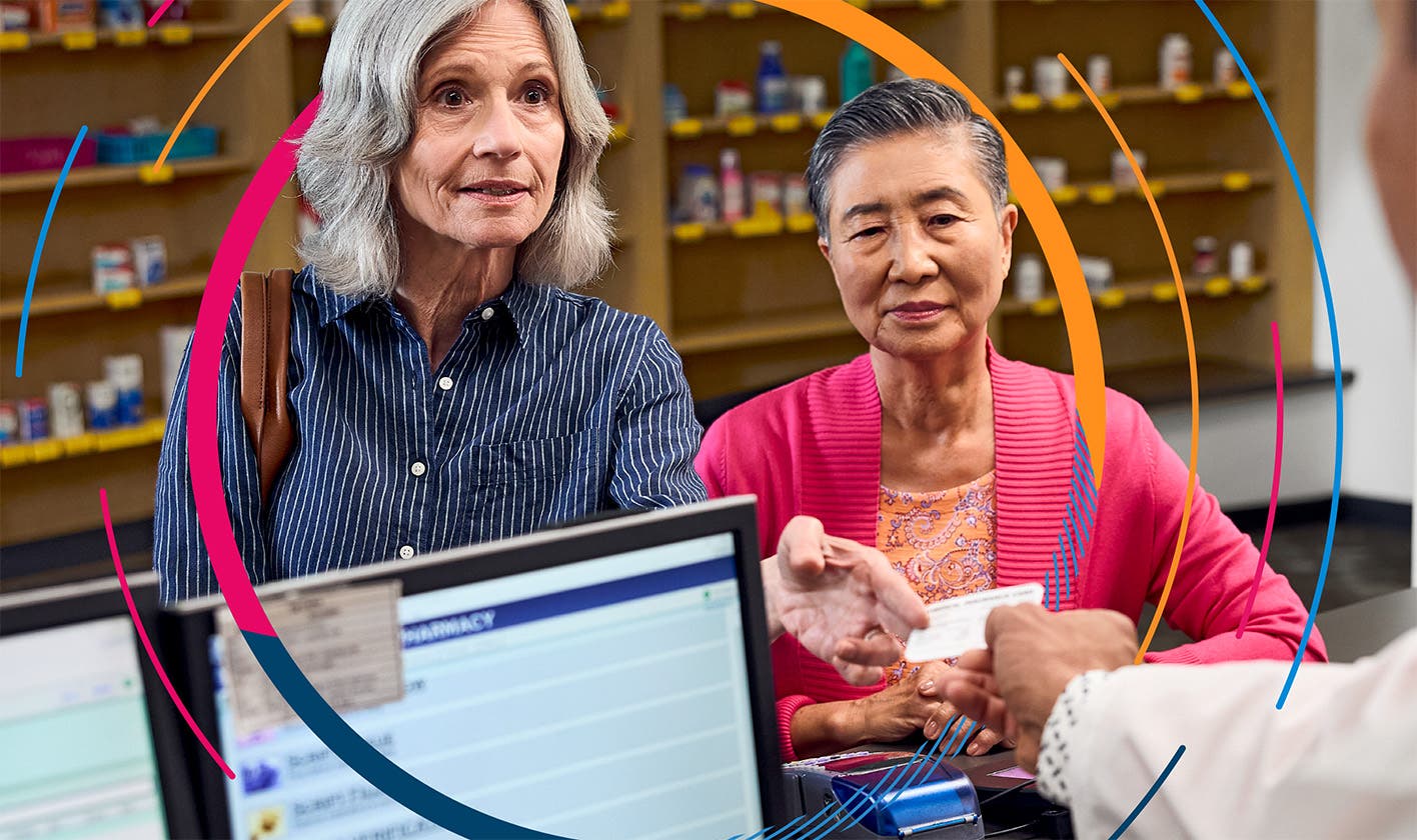 A patient and their spouse at the pharmacy counter, presenting an insurance card to the pharmacist to process a prescription payment.